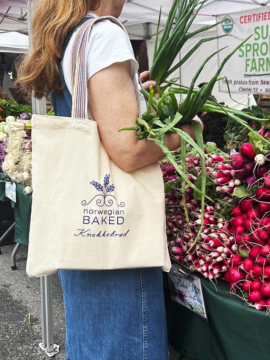 Woman carrying Norwegian Baked tote bag at farmers market with fresh produce